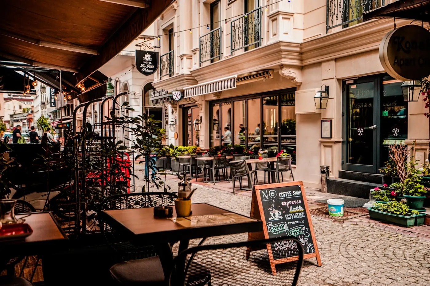 Straßenansicht eines Café-Eingangs mit Tischen draußen und Tafel-Schild „Coffee Shop“