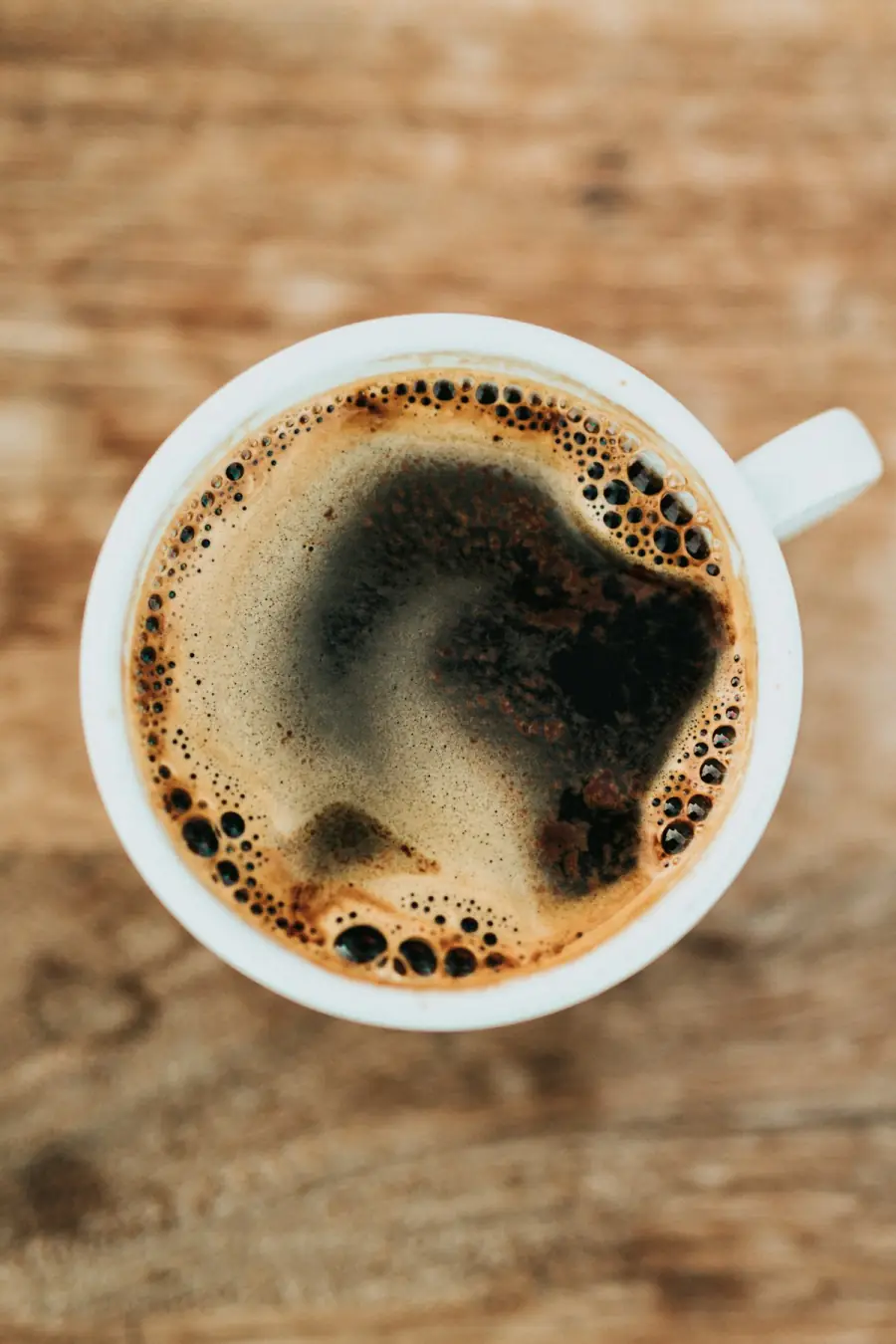 Tasse schwarzer Filterkaffee von oben, frische Crema auf dunklem Holztisch