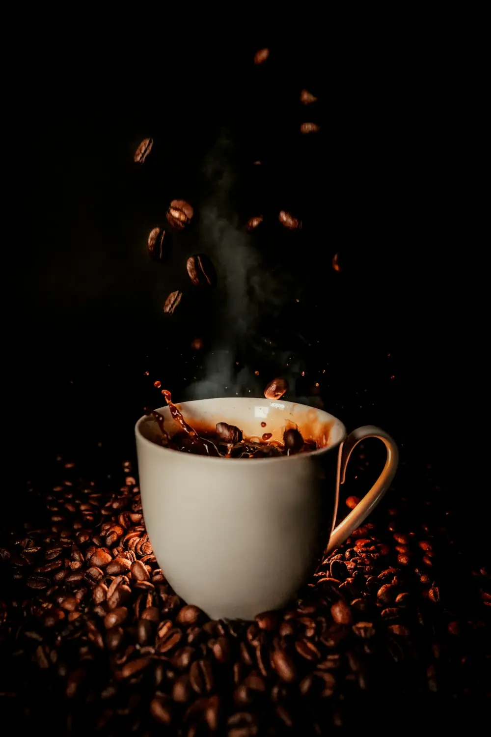 Dunkle, stimmungsvolle Aufnahme: dampfender Kaffee und fallende Röstbohnen über einer Tasse